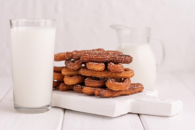 Homemade churros with milk and cream on a white wooden background