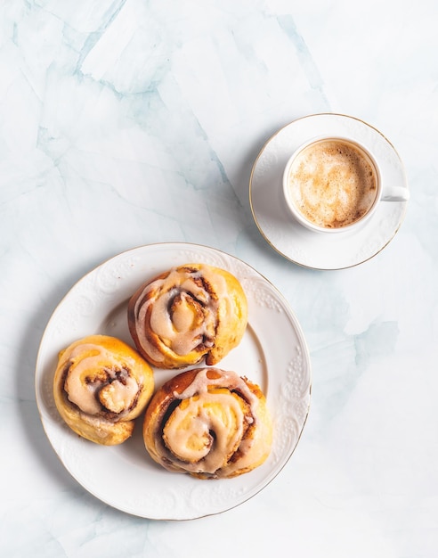 Homemade cinnamon rolls on a white plate and a cup of coffee on a white table