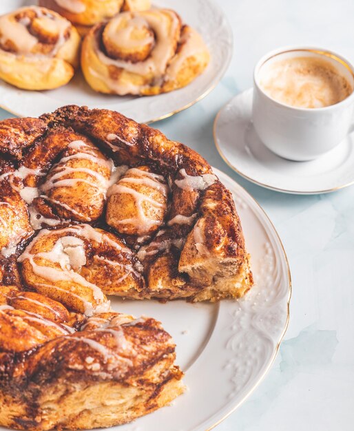 Panini alla cannella fatti in casa su un piatto bianco su un tavolo bianco con caffè e panini di pasticceria per colazione