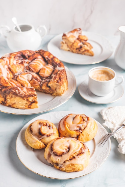 Rotoli di cannella fatti in casa su un piatto bianco su un tavolo bianco con caffè e focacce per la colazione