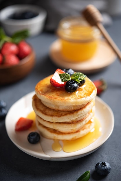 Homemade classic American pancakes in a stack with fresh berries and honey closeup on a blurry dark ...