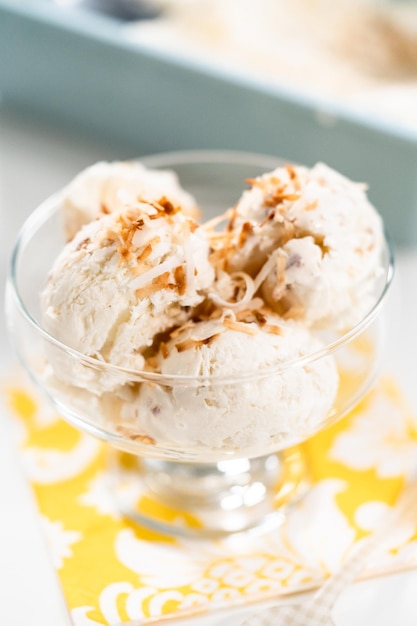 Homemade coconut ice cream garnished with roasted coconut flakes in a glass ice cream bowl