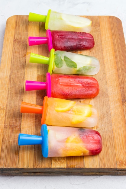 Homemade colorful fruity popsicle on a wooden board and against