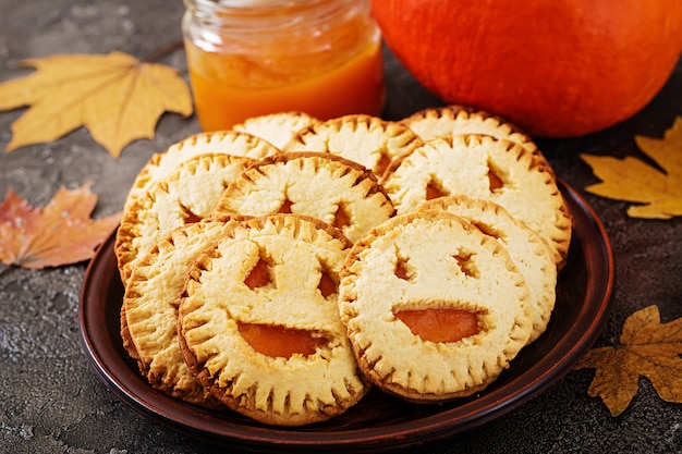 Homemade cookies in the form as Halloween jack-o-lantern pumpkins on the dark table.