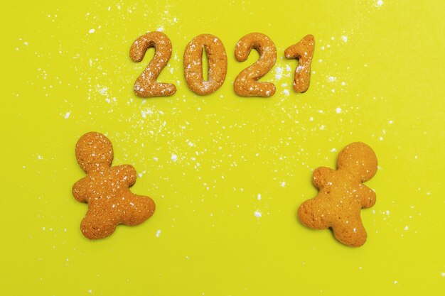 Homemade cookies in the form of numbers 2021 and two gingerbread men on a yellow background, top view, flat lay, copy space. Christmas food background