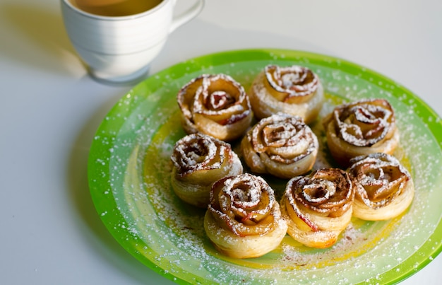 Homemade cookies roses with a sugar powder on colorful plate and a latte cup. Breakfast and dessert concept.