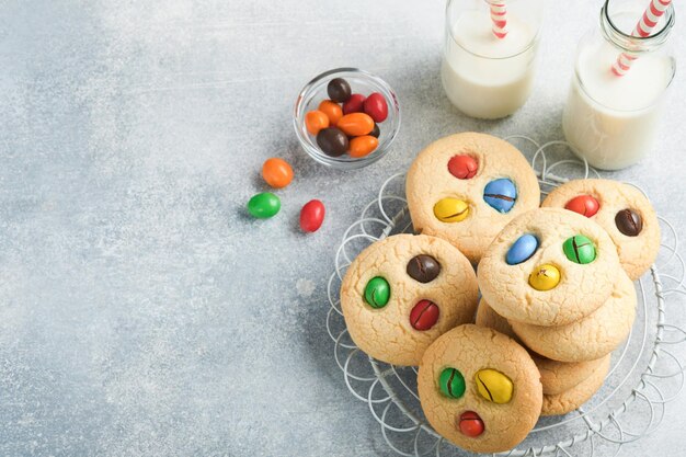 カラフルなチョコレート菓子とミルクの自家製クッキーライトグレーの背景にミルクのボトルとプレート上のマルチカラーキャンディーとショートブレッドクッキーのスタックベビーフードのコンセプトコピースペース