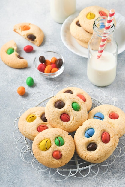 Homemade cookies with colorful chocolate candies and milk Stack of shortbread cookies with multi colored candy on plate with bottle of milk on light gray background Baby food concept Copy space