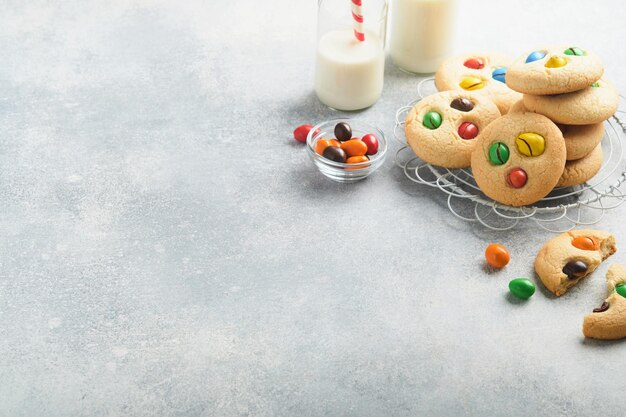 Homemade cookies with colorful chocolate candies and milk Stack of shortbread cookies with multi colored candy on plate with bottle of milk on light gray background Baby food concept Copy space