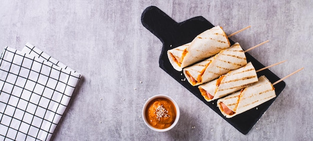 Homemade corn dogs in grilled tortilla with sauce on slate on the table top view web banner