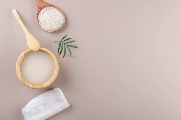 Homemade cosmetic rice water with ingredients and beauty kit on beige background top view copy space