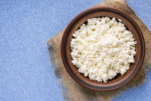 Homemade cottage cheese in a bowl on a sack and on a blue table.