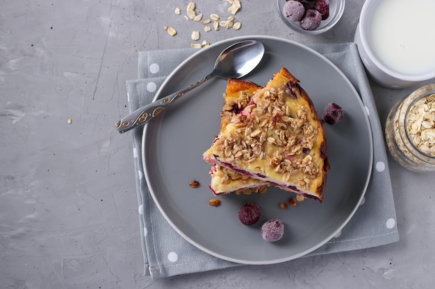 Homemade cottage cheese casserole with oatmeal and cherry on a gray plate on a light gray background