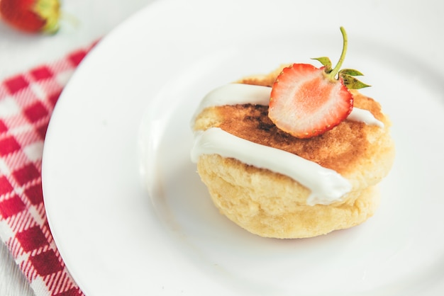 Homemade cottage cheese pancakes with sour cream and fresh strawberry on white wooden background.