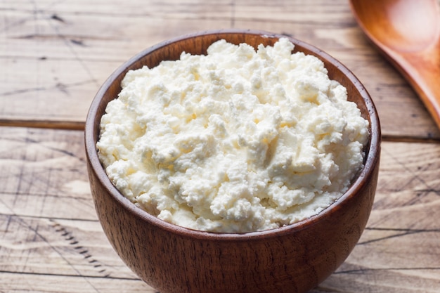 Homemade cottage cheese in a wooden bowl on old wooden table.
