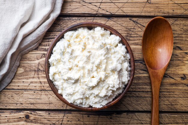 Homemade cottage cheese in a wooden bowl on old wooden table.