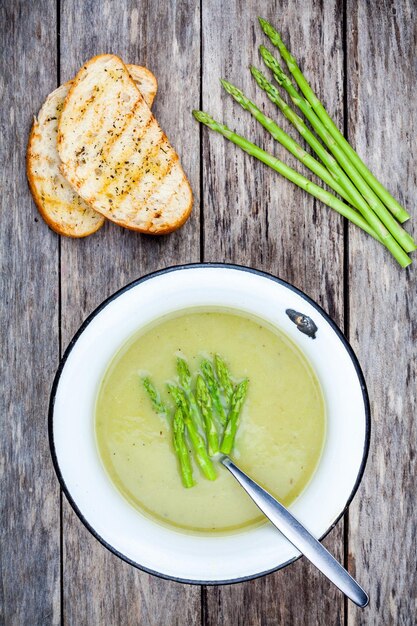 Homemade cream soup with asparagus and toasted ciabatta on rustic background