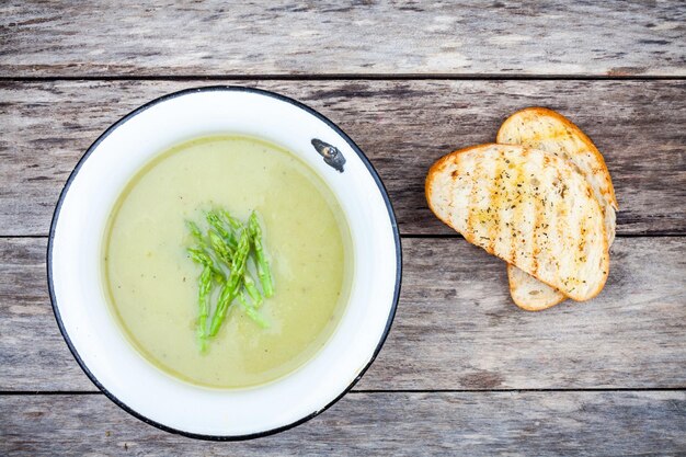 Homemade cream soup with asparagus and toasted ciabatta on rustic background