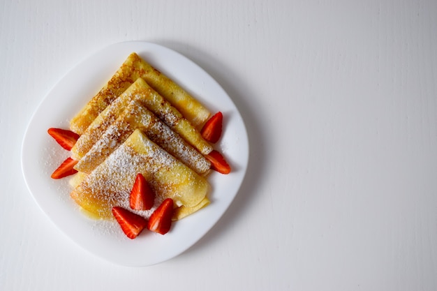 Homemade crepes, tasty thin pancakes with strawberry and powdered sugar on white plate