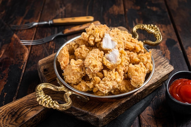 Homemade crispy popcorn chicken bites in a skillet wooden\
background top view