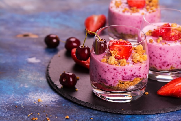 Homemade crubmle dessert with fresh berries and yogurt in glasses on wooden background