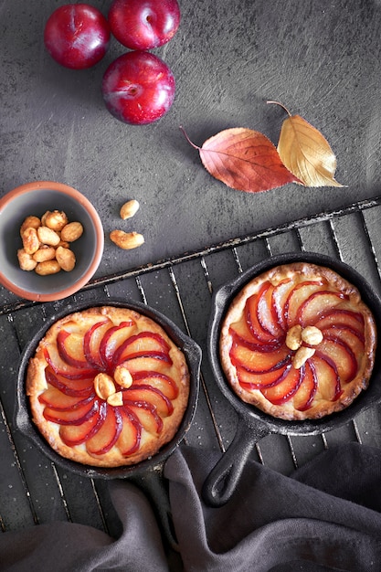 Homemade crumble tarts with plum slices baked in small iron skillets