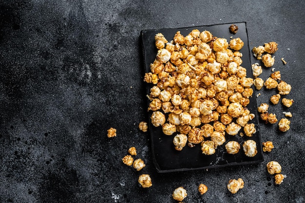 Homemade Crunchy Caramel Popcorn on marble board. Black background. Top view. Copy space.