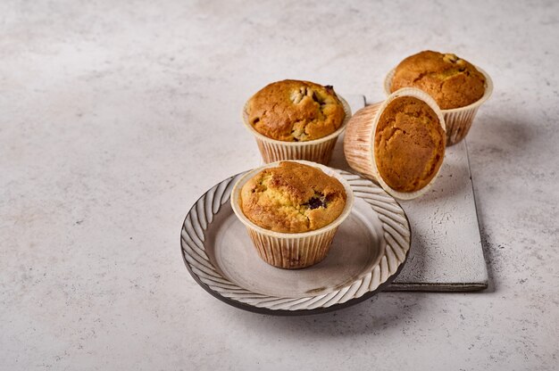 Homemade cupcakes in baking paper forms on plate and scratched ceramic cutting board on gray