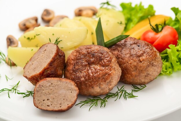 Homemade cutlets with potatoes and vegetables on a white background.