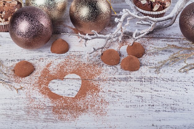 Homemade dark chocolate truffles with heart shaped cocoa powder and winter decoration on white rustic wooden table. Winter holiday background. Flat lay with copy space for text.