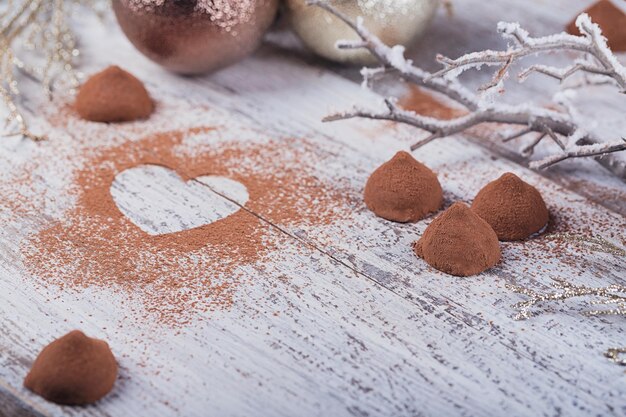 Homemade dark chocolate truffles with heart shaped cocoa powder and winter decoration on white rustic wooden table. Winter holiday background.