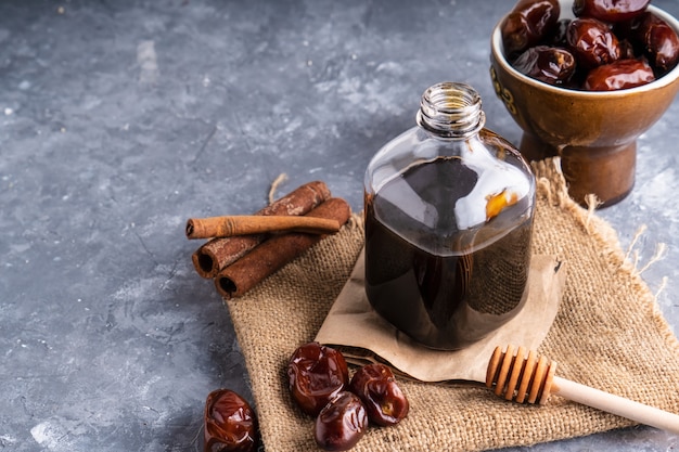 Homemade dates syrup in glass bottle on gray stone table. 