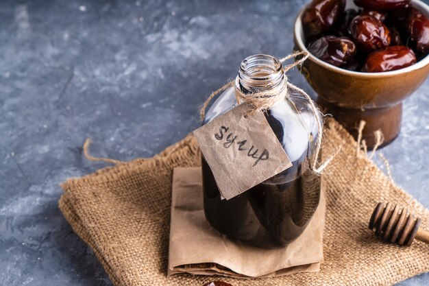 Homemade dates syrup in glass bottle on gray stone table. 