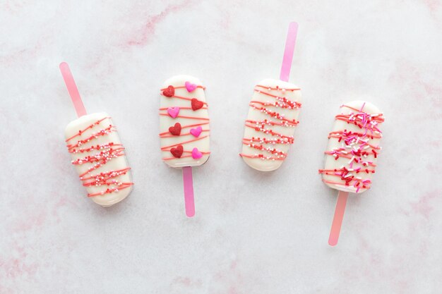 Homemade decorated cakesicles for valentines day on a pink marble surface