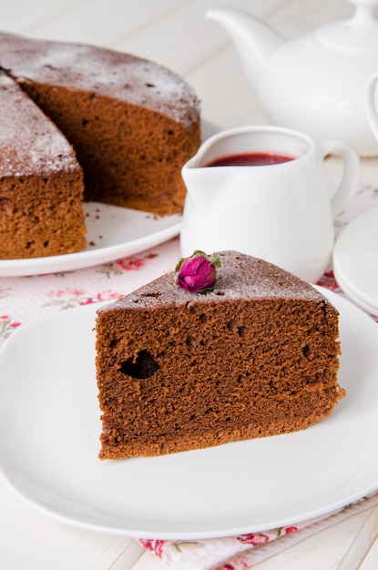 Homemade delicious chocolate sponge cake powdered with sugar powder on a white plate on a wooden table.