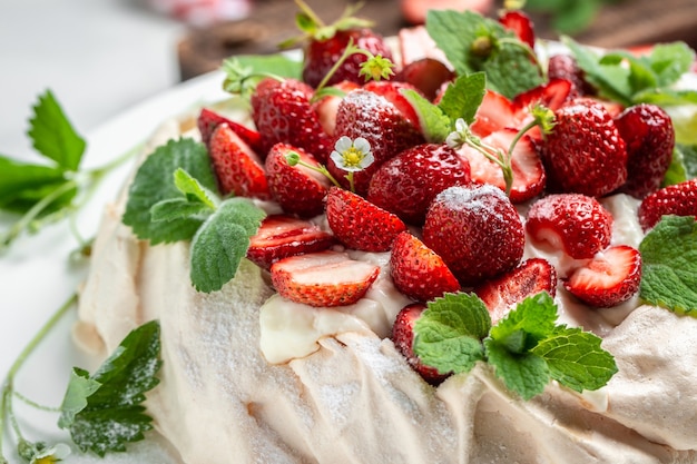 Homemade delicious meringue cake Pavlova with whipped cream, fresh strawberries and mint