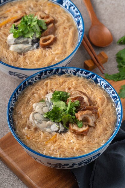 暗い木製のテーブルの背景にボウルに自家製のおいしい牡蠣と大腸春雨の細い麺。