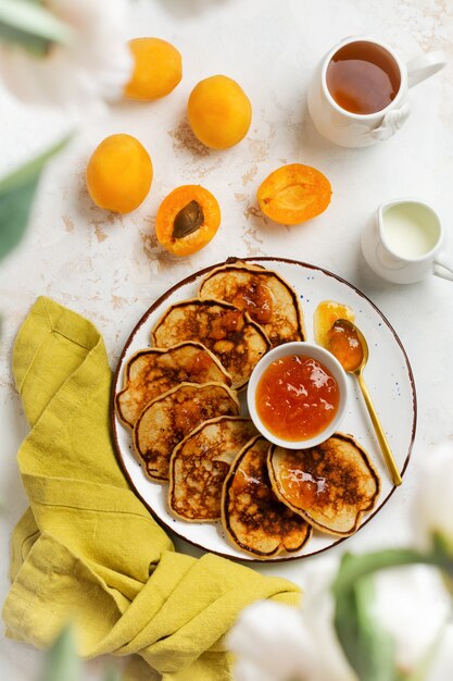 Homemade delicious pancakes with fresh apricot fruit and jam on a light slate, stone or concrete wall. Top view with copy space.