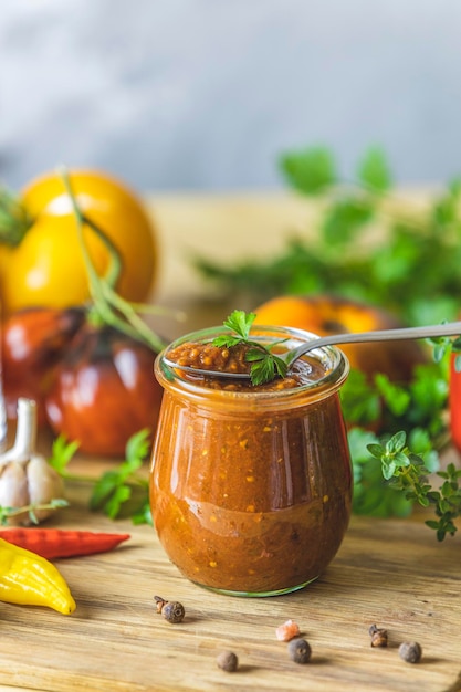 Homemade DIY natural canned hot plum sauce chutney with chilli or tkemali in glass jar standing on wooden table with ingredients Selective focus