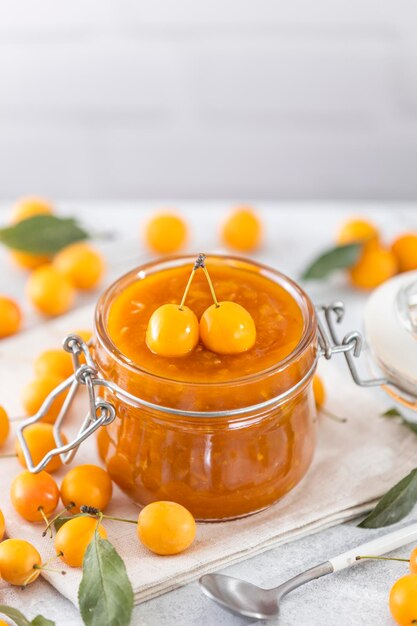 Homemade diy natural canned yellow cherry plum sauce chutney with chilli or tkemali in glass jar standing on white table selective focus