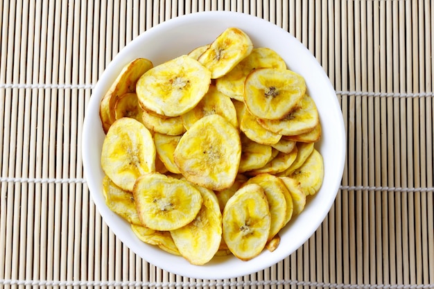 Homemade dried banana chips in ceramic bowl top view