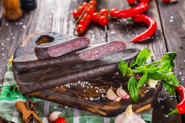 homemade dried sausage, whole and in pieces, spices and vegetables on a kitchen cutting board, dark