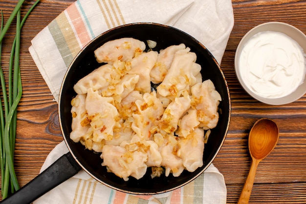 Homemade dumplings vareniki varenyky pyrohy with stewed cabbage fried with onion on panTraditional ukrainian popular national dishcuisine served with sour cream on wooden board