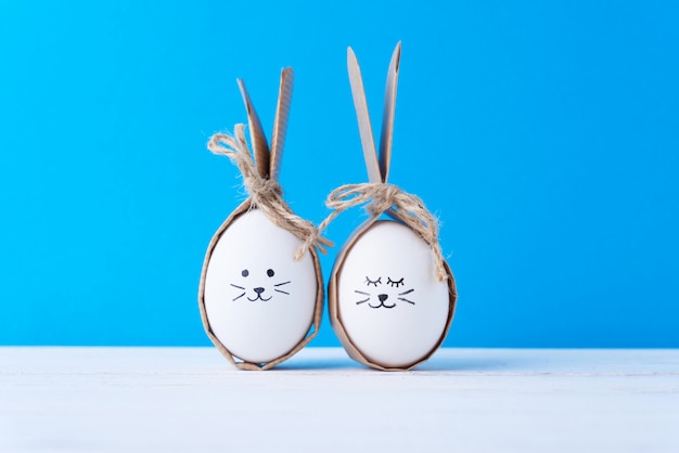 Uova di pasqua fatte in casa con facce e orecchie di coniglio su sfondo blu. concetto di pasqua