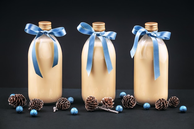 Домашний гоголь-моголь в бутылках с сосновыми шишками и синими шариками на темном фоне