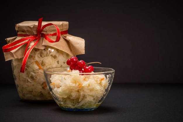 Homemade fermented cabbage in a glass bowl and a jar in the black background Vegan salad