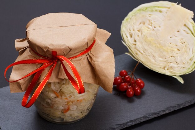 Homemade fermented cabbage with carrot in glass can. Fresh head of cabbage and cluster of viburnum on the background. Vegan salad. Dish is rich in vitamin U. Food great for good health.