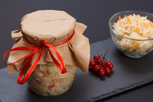 Homemade fermented cabbage with carrot in glass jar and bowl, cluster of viburnum on the background. Vegan salad. Dish is rich in vitamin U. Food great for good health.