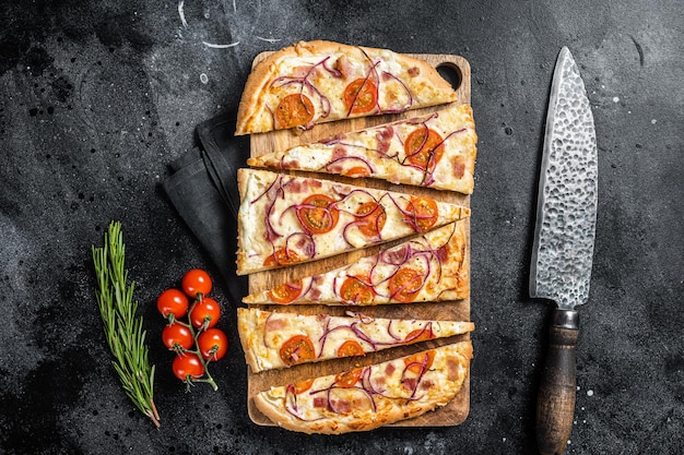 Homemade Flammkuchen or tarte flambee with cream cheese, bacon, tomato and onions. Black background. Top view.