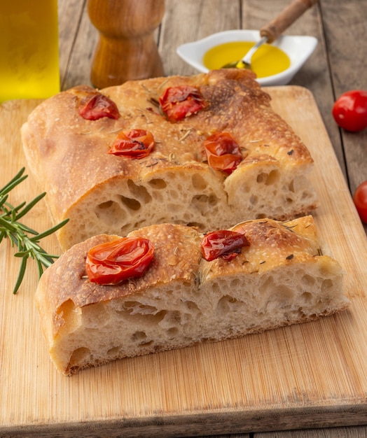 Homemade focaccia with cherry tomato, garlic, olive oil and rosemary over wooden table.